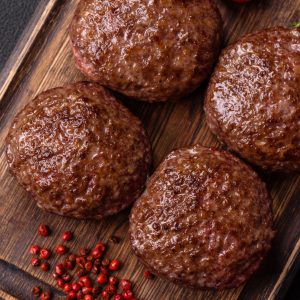Beef burger patties with salt, spices and herbs grilled on a dark concrete background